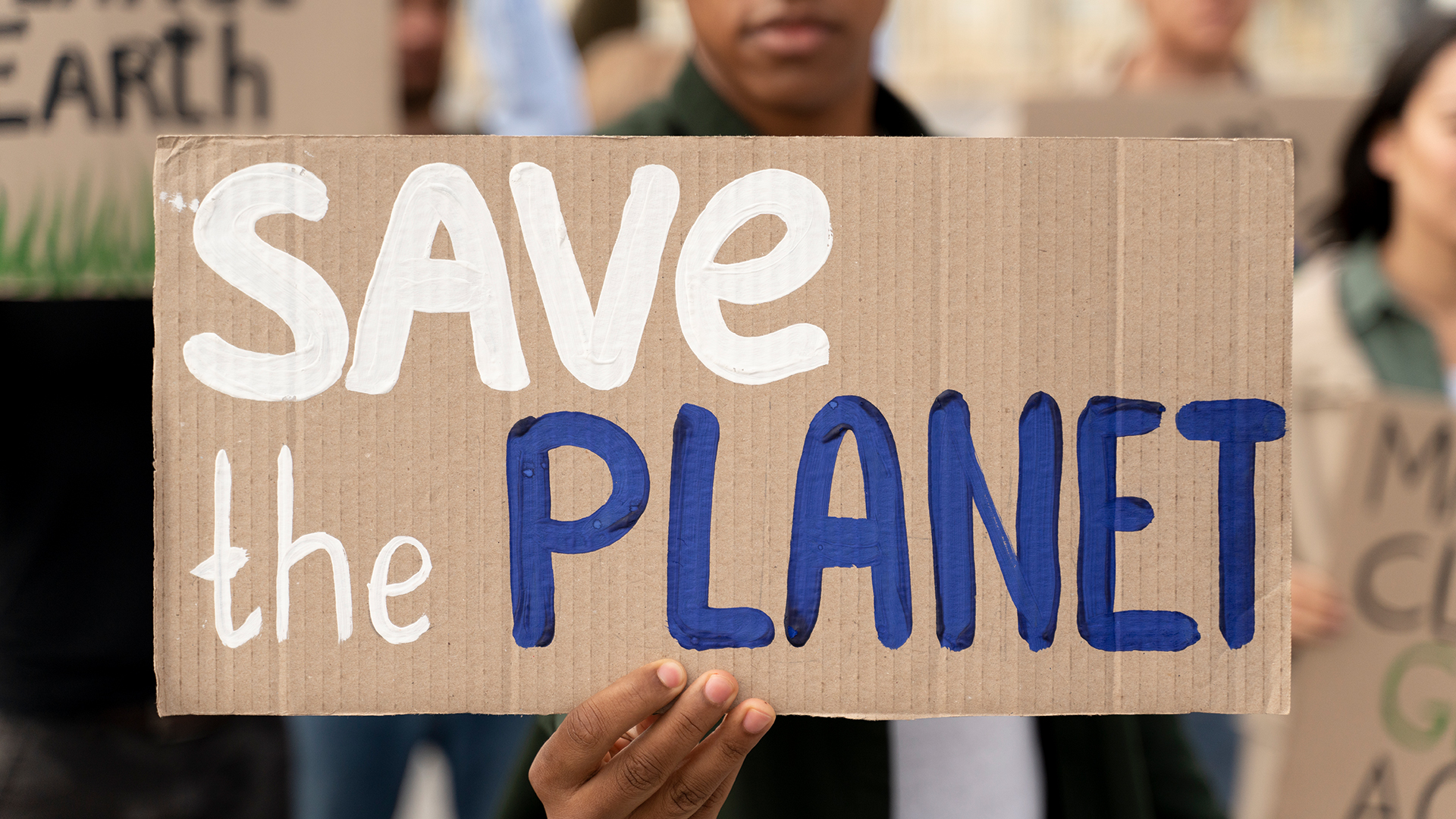 An activist holds a Save the Planet sign on cardboard to the camera