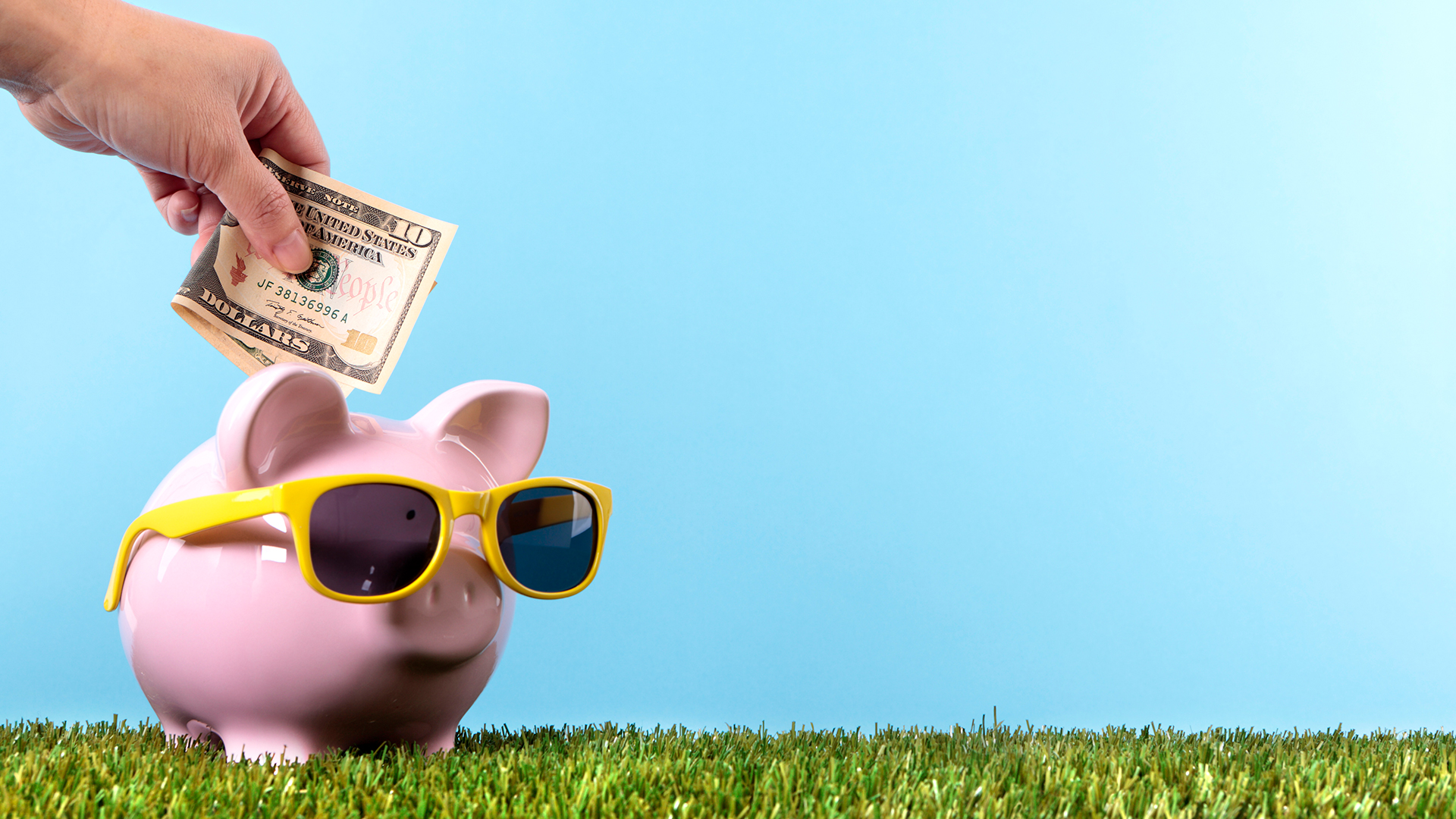 Someone putting a $10 bill into a piggy bank